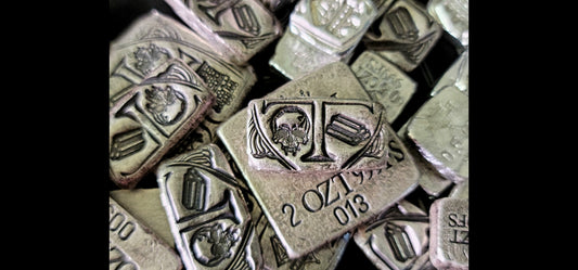 1 oz Trials/Treasure Bar in .999 fine silver shown over a 2 oz Kannibal Hektor Crest Bar among other hand-cast silver pieces